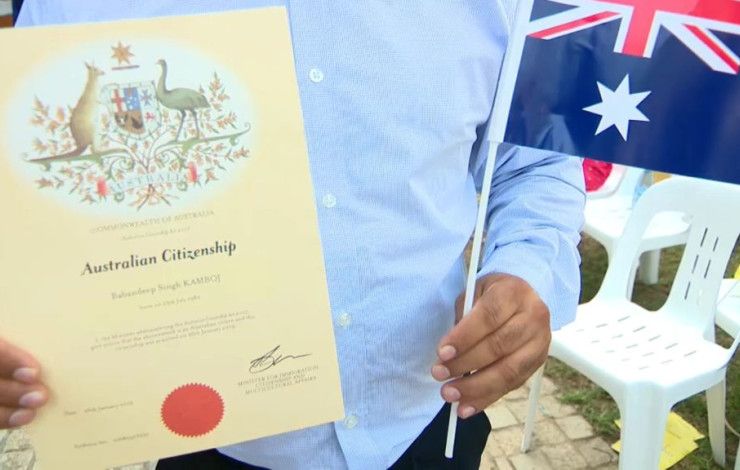 a person holding a Citizenship certificate and an Australian flag