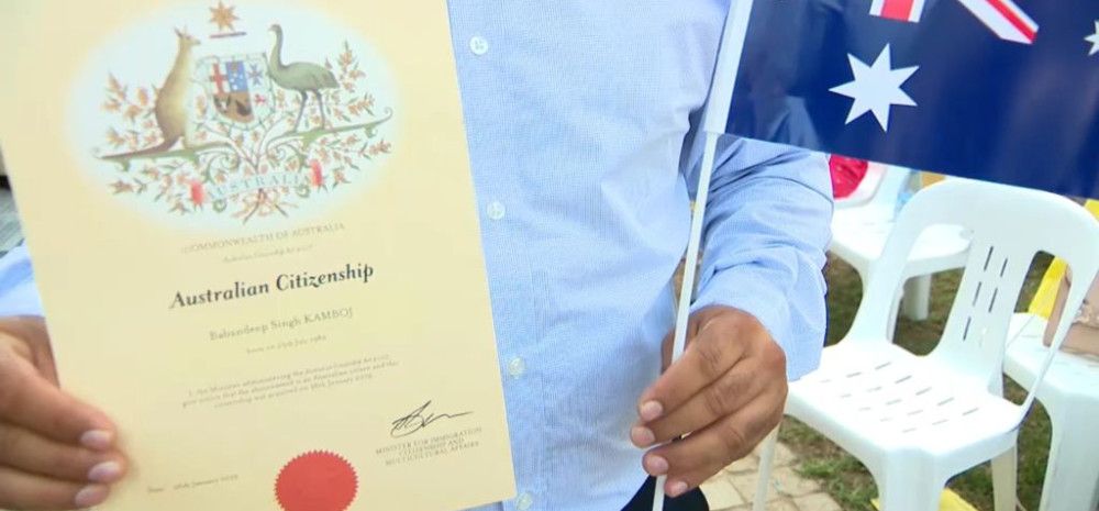 a person holding a Citizenship certificate and an Australian flag